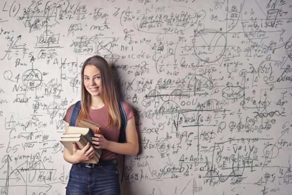Studentessa sorridente con zaino e libri davanti a una parete piena di formule matematiche, simbolo dell’impegno in un liceo paritario